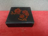 an old black box with red flowers on it sitting on a red surface