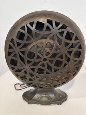 un vieux ventilateur en métal posé sur un pied, sur une surface blanche