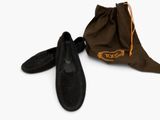 une paire de pantoufles en daim noir et un sac fourre-tout posés sur une surface blanche