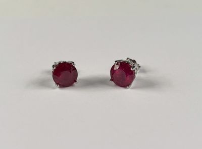 une paire de boucles d'oreilles à clous ornées de rubis, posées sur un fond blanc