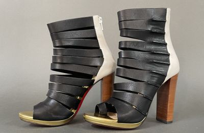 black and white high heeled sandals with gold accents on a grey background