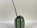 a small green vase with a long stick sticking out of it