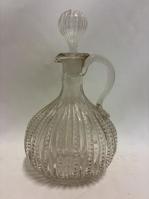 une bouteille en verre transparent munie d'une anse, posée sur une surface blanche