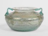 un vase en verre vert muni d'anses, posé sur une surface blanche