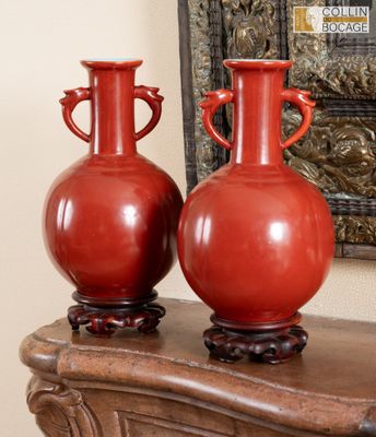 deux vases rouges posés sur une table en bois, à côté d'un miroir