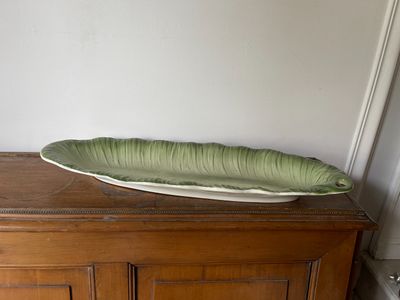 un grand plat vert en forme de feuille posé sur un meuble en bois