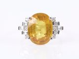 a close up of a yellow sapphire and diamond ring on a white surface