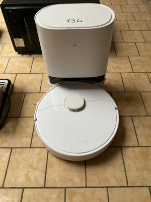 un robot blanc posé sur un sol carrelé, à côté d'un micro-ondes