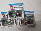 trois figurines Nintendo Mario Kart dans leurs boîtes, posées sur une surface blanche
