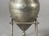 a silver vase that is on a stand on a gray surface