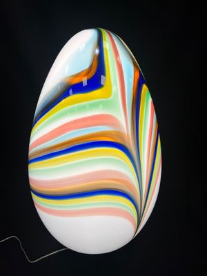 un œuf en verre aux couleurs vives sur fond noir, avec un fil métallique au premier plan