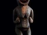 une statue en bois représentant un singe la bouche ouverte, sur fond noir