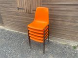 une pile de chaises orange posée contre un mur en bois