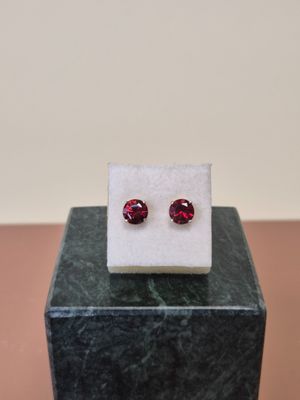 une paire de boucles d'oreilles ornées de grenats rouges, posées sur un bloc de marbre
