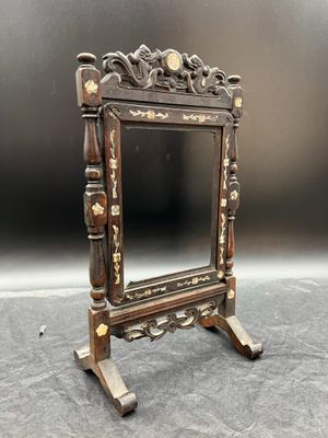 un miroir ancien en bois posé sur un pied, sur une surface grise