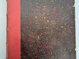 un vieux livre posé sur une table blanche à côté d'un livre rouge