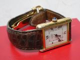 une petite montre posée sur un fond rouge, avec un bracelet doré