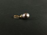 un pendentif en forme de perle argentée muni d'un fermoir en or, sur un fond noir