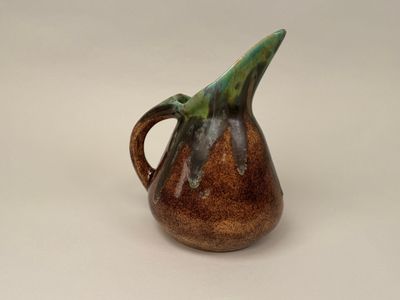 un pichet marron avec une anse verte sur un fond blanc