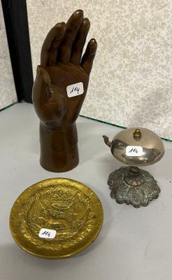 une main en bois tenant une assiette en or, à côté d'autres objets en laiton