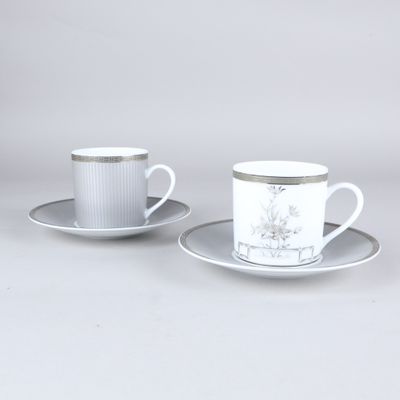 two cups and saucers with silver rims are sitting on a table