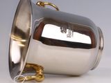 a silver cup with a gold handle on a white surface