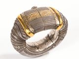 un gros plan d'un bracelet en argent rehaussé de touches dorées sur fond blanc