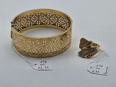 a close up of a gold bracelet and a ring on a white surface