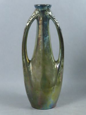 a green glass vase with a metal handle on a gray background