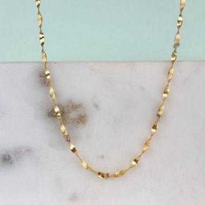 un gros plan d'un collier en or posé sur une surface en marbre
