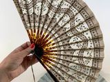 a woman holding a paper fan with a tassel on it