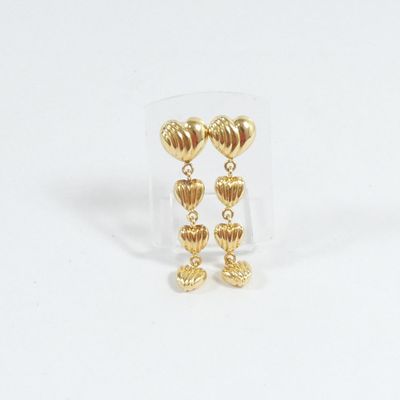 une paire de boucles d'oreilles en or en forme de cœur, présentées dans une boîte transparente posée sur un fond blanc
