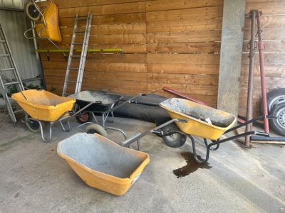 Plusieurs brouettes sont alignées dans un garage, à côté d'une échelle
