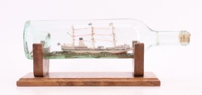 un bateau dans une bouteille, posé sur un socle en bois, sur fond blanc