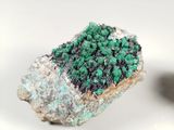 green and black crystals on a white surface next to a rock