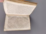 someone is holding an open book in their hand on a table