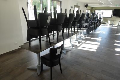 Des tables et des chaises sont alignées dans une grande pièce dotée de fenêtres
