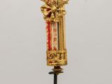 un objet doré et rouge posé sur un socle, sur une table en bois