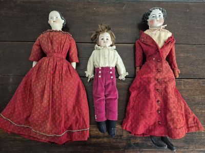 trois poupées anciennes représentant des femmes en robe rouge, couchées les unes à côté des autres