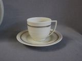 a cup and saucer on a table with a clock in the background