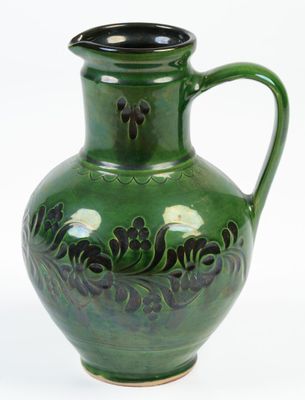 un vase vert muni d'une anse noire, posé sur une surface blanche