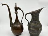 two antique metal pitchers sitting next to each other on a white surface
