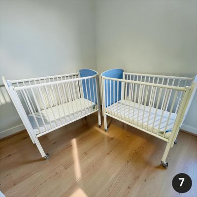 deux lits bébé dans un coin d'une pièce au sol en parquet