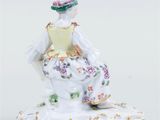 porcelain figurine of a woman in a dress and hat sitting on a rock