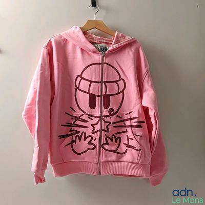 un sweat à capuche rose avec un chat dessiné dessus, accroché au mur