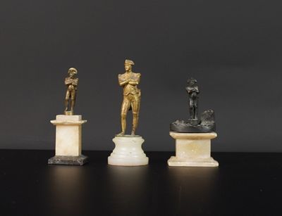 trois statues en bronze représentant un homme et une femme, posées sur des socles en marbre
