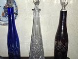 trois vases en verre posés sur une table où se trouvent également des assiettes et une horloge