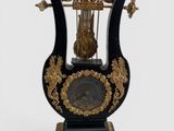 une horloge noire et dorée surmontée d'une cage à oiseaux