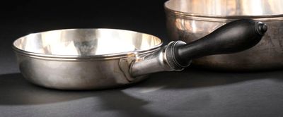 un bol en argent et une poêle en argent posés sur une table noire