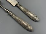 une paire de couteaux plaqués argent et un couteau posés sur une surface grise